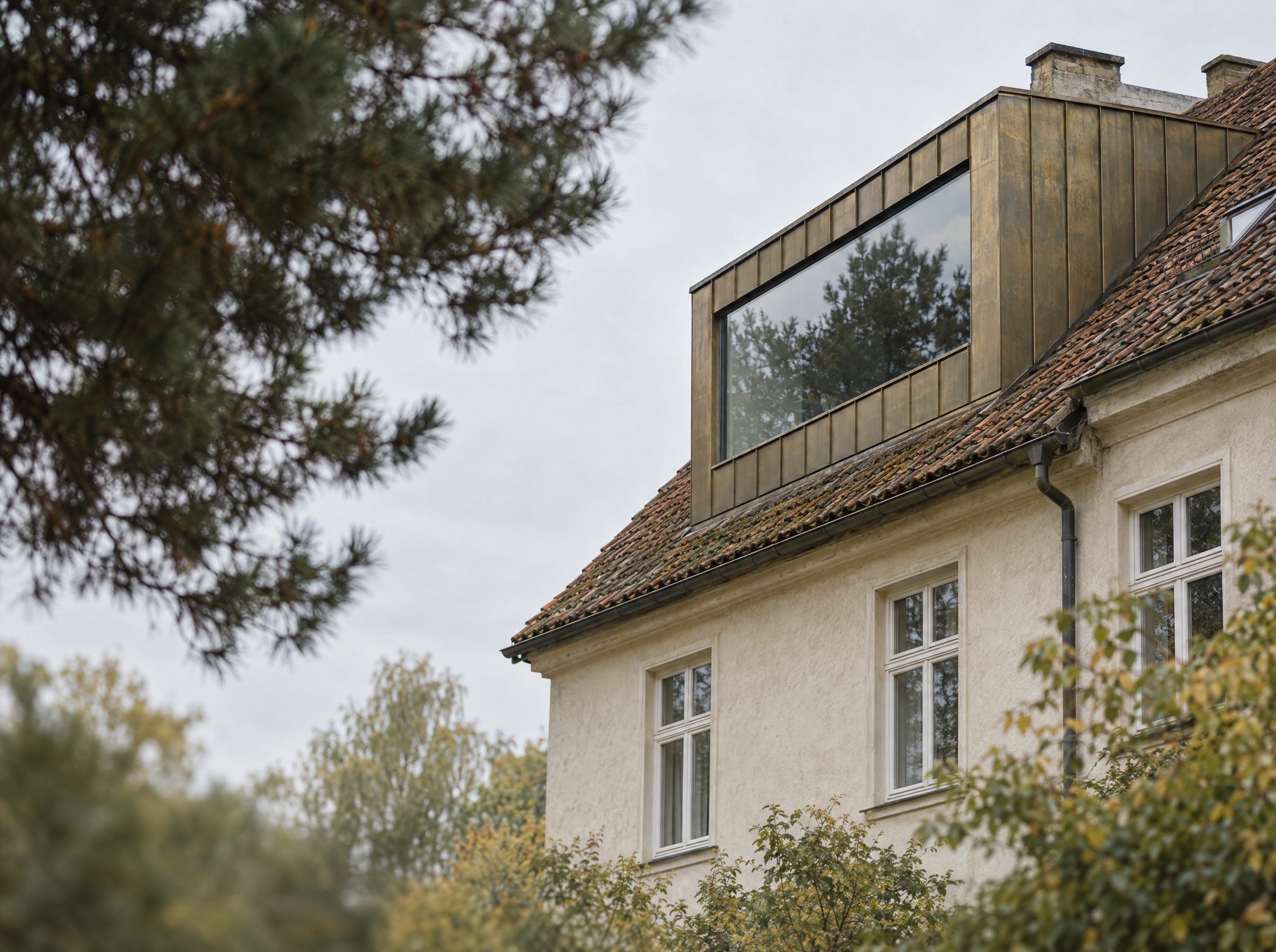 Bestandshaus mit neuer Dachgaube aus Messing, hinter Kiefern