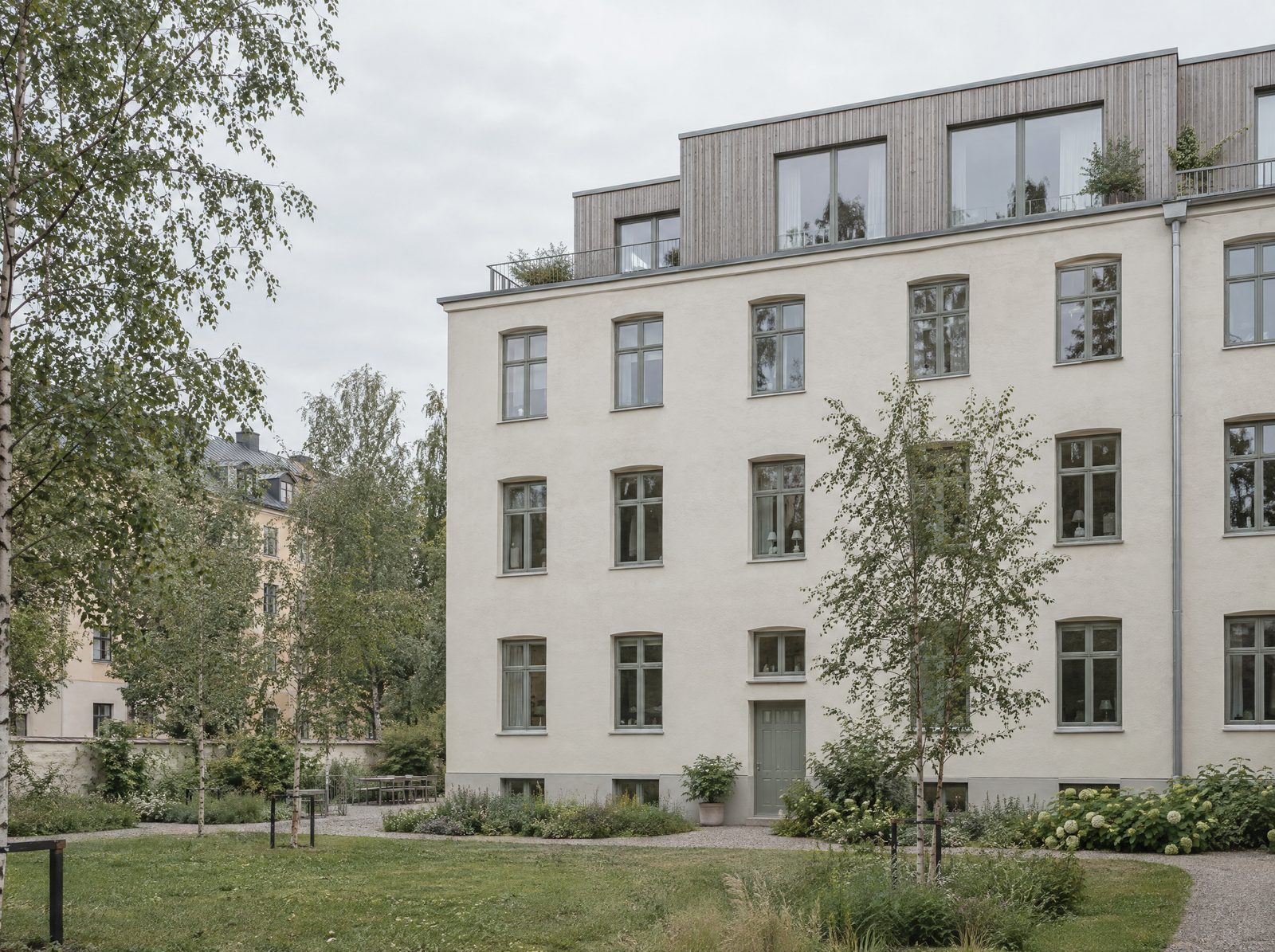 Saniertes Mehrfamilienhaus mit hellem Putz und neuem Dachgeschoss aus Holz, vom begrünten Innenhof mit Birken